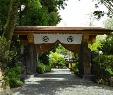 Traditional wooden gateway with noren curtains leading to a gravel garden path at Ochiairo ryokan in Shizuoka, Chūbu, Japan