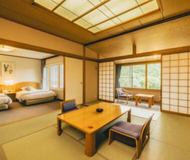 Traditional tatami room with low wooden table, shoji screens and adjoining sleeping area with beds and greenery outside window