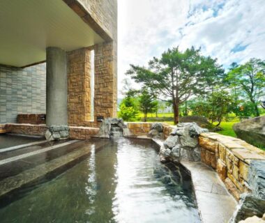 Stone-edged outdoor onsen bath overlooking a landscaped garden at Oehonke, Hokkaidō