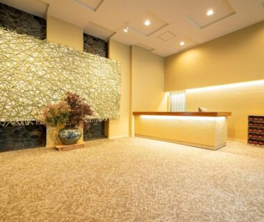 Ryokan reception with lit desk, decorative wall panel, carpeted floor and flower arrangement at Ogiwarakan, Nagano