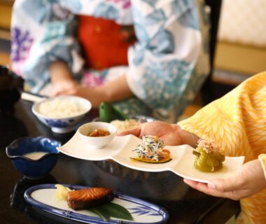 Hands serving small plated dishes to guests in kimono at Ogiwarakan, Chūbu, Nagano, Japan