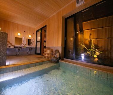 Tiled indoor onsen bath with wooden ceiling, glass doors and a small seating area at Ohanabo in Kyoto
