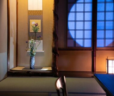 Traditional tatami room with round shoji window, tokonoma alcove with vase and hanging scroll, soft lantern lighting