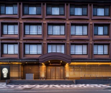 Evening exterior of multi-story hotel with illuminated entrance and wooden lattice frontage in Yamanashi