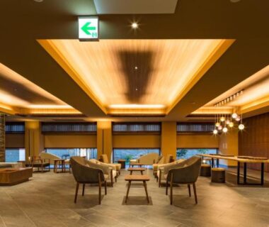 Spacious hotel lounge with sofas, low wooden tables, warm ceiling lighting and wide windows at Oike Hotel, Yamanashi