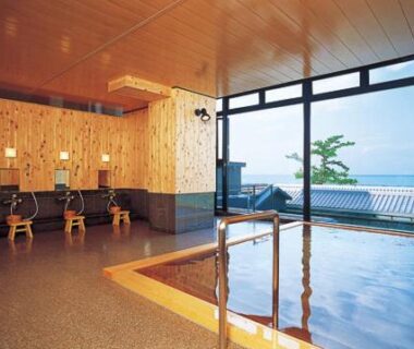 Indoor onsen with wooden interior, washing stations and large windows overlooking the sea at Oishiya, Mie