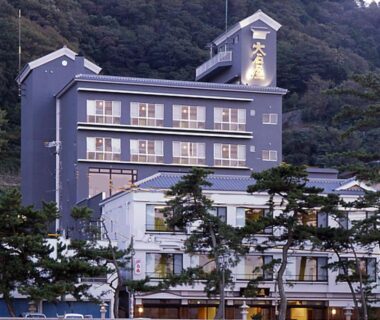 Multi-story ryokan building with balconies and pine trees at the foot of a forested hillside in Mie, Kansai