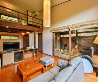 Loft living area with sofa, wooden table, staircase and glass doors revealing a wooden bath and courtyard greenery