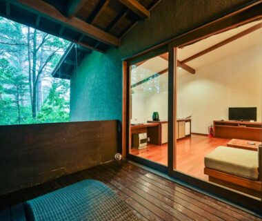 Sliding glass doors from a low-seated room to wooden veranda overlooking verdant forest at Oita Kuoritei Kyushu