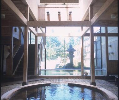 Circular indoor onsen bath with wooden beams and windows overlooking stone lantern garden at Okada Ryokan Warakutei Gifu