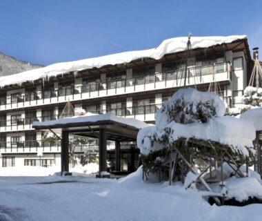 Multi-story snow-covered ryokan with entrance canopy and forested mountain backdrop in Gifu, Chūbu