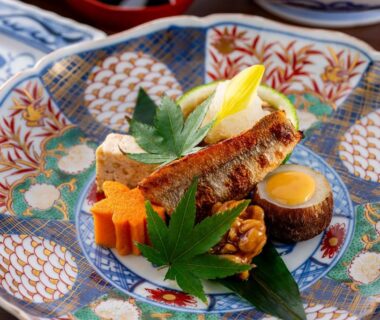 Grilled fish and assorted small dishes on ornate porcelain plate with decorative maple leaves