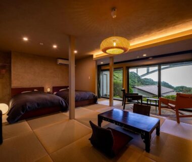 Tatami room with low table, twin beds and balcony overlooking green hills at Okamotoya Ōita