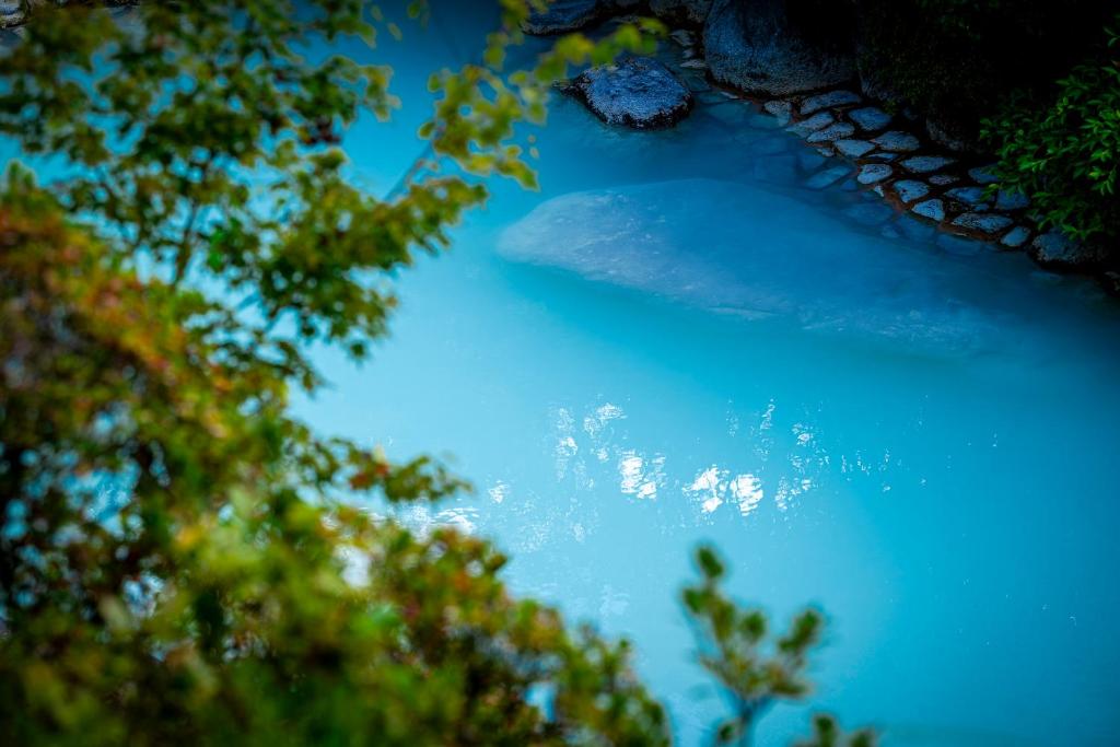 Milky Blue Onsen at Okamotoya Ōita Milky turquoise onsen water with stone edging and lush greenery at Okamotoya in Ōita, Kyūshū