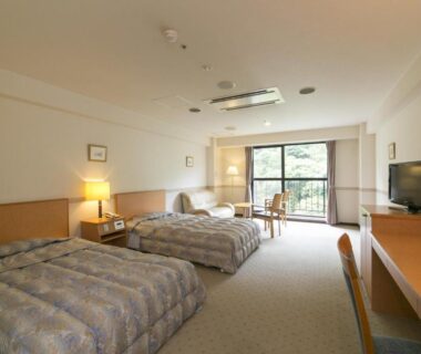 Twin bedroom with two beds, desk, TV and balcony overlooking trees at Okuhida Garden Hotel Yakedake in Gifu