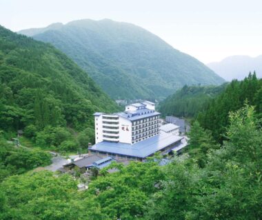White multi-story ryokan nestled in a forested valley surrounded by green mountains, Okuhida Garden Hotel Yakedake Gifu