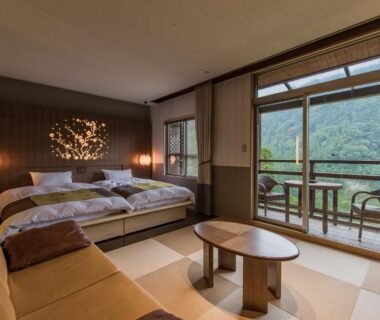 Tatami room with low beds, sofa and balcony overlooking green mountains at Okuhita Onsen Umehibiki Ōita