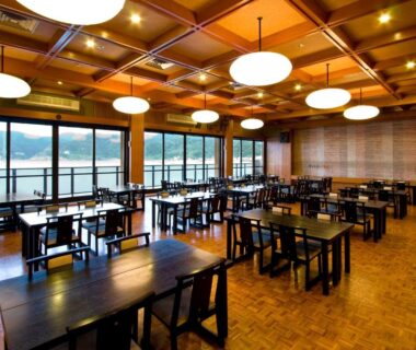 Spacious dining room with wooden tables and large waterfront windows at Okukinosaki Seaside Hotel Hyōgo Japan