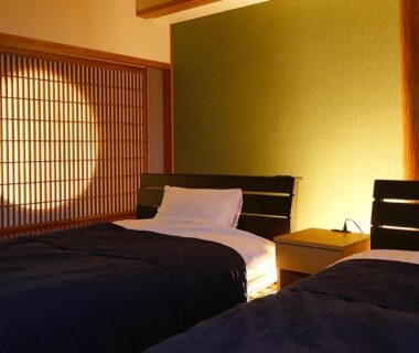 Twin beds beside circular shoji light and wooden nightstand in a calm room at Okukinosaki Seaside Hotel, Hyōgo