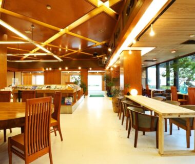 Spacious wooden lounge with communal tables and large windows overlooking greenery at Okukinosaki Seaside Hotel Hyōgo