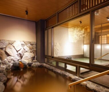 Stone-lined indoor onsen bath with wooden handrail and glass partition at Okuno Hosomichi in Hyogo, Kansai