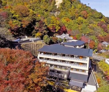 Multi-story ryokan building on forested hillside with autumn foliage in Hyōgo Japan