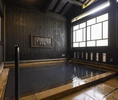 Calm indoor onsen with dark wood walls and shoji-style windows at Okyakuya, Kumamoto, Kyushu, Japan