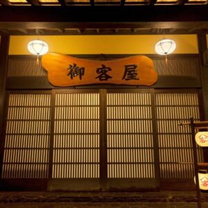 Warm lantern-lit wooden facade with slatted shoji doors and Okyakuya signboard in Kumamoto, Kyushu