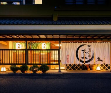 Warmly lit traditional ryokan entrance with noren curtain and wooden facade at Omori, Gunma