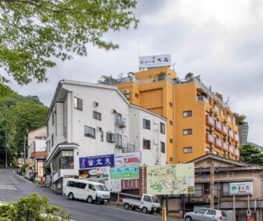 Multi-story ryokan buildings on a sloped street with parked vans and signage in Gunma, Japan