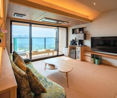 Tatami-floored guest room with low table, sofa and large window framing water and distant mountains at Omori, Gunma, Kanto