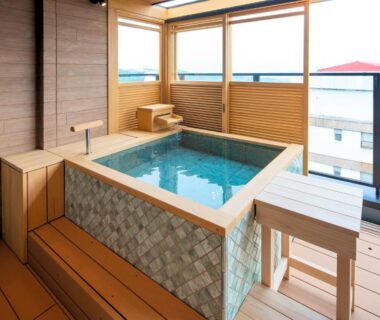 Indoor wooden bathing tub with mosaic tiles, bench seating and balcony view at Omori ryokan in Gunma