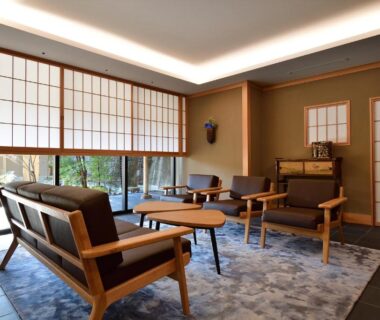 Lounge with shoji screens, wooden seating and low tables overlooking a garden at Oni no Sumika in Shizuoka