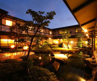 Lit central courtyard pond with wooden corridors and traditional rooms at Onishiya Suishoen in Hyōgo