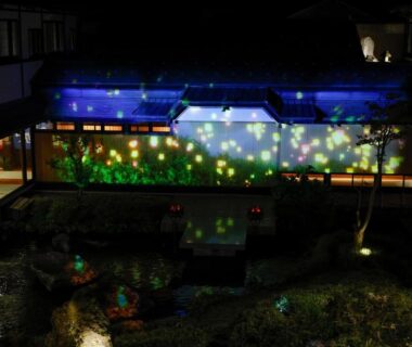 Nighttime courtyard garden with illuminated wall projections and pond at Onishiya Suishoen in Hyōgo