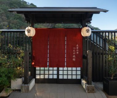 Red noren curtain and lanterns at a traditional wooden ryokan entrance with mountain backdrop in Kanagawa