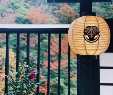 Paper lantern on veranda with shoji screen and autumn foliage beyond at Onsen Guest House Tsutaya, Kanagawa