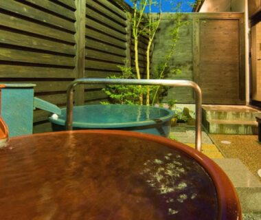 Round wooden tub and stone onsen area with handrail, bench and privacy slats at Onsen Urashima, Hiroshima