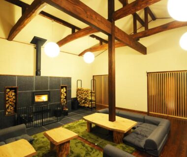 High-ceiling lounge with exposed wooden beams, low tables and wood stove at Onsen Yado Misuzuso in Nagano, Chūbu