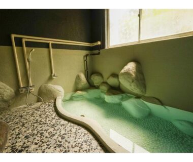Stone-lined indoor onsen bath with window and hand showers at Onsen Yado Mizuguchi, Shizuoka