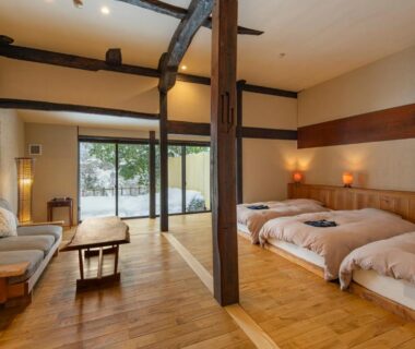 Low beds, wooden beams and sliding glass doors opening to garden at Onsen and Garden Nana, Ishikawa