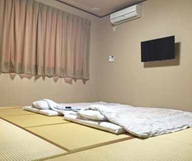 Simple tatami room with futons, wall-mounted TV and air conditioner at Onsenminshuku Kosakaya, Wakayama