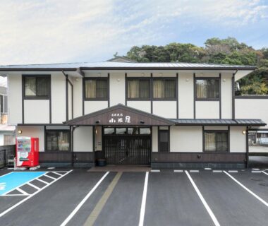 Two-story white exterior with entrance canopy, marked parking bays and vending machine, Onsenminshuku Kosakaya, Wakayama, Kansai