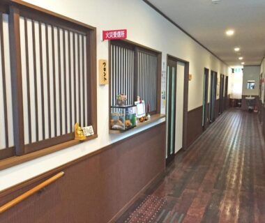 Interior hallway with wooden floors, shoji lattice windows and reception counter at Onsenminshuku Kosakaya, Wakayama