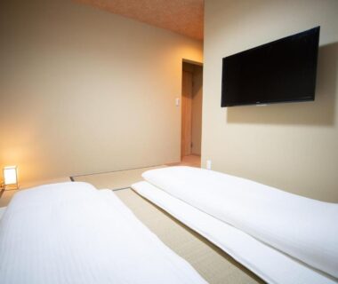 Minimal tatami room with two futons, wall-mounted TV and soft corner lighting at Onya Kaede Kyoto