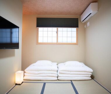 Minimal tatami room with stacked futon, shoji window, wall TV and floor lantern at Onya Kaede in Kyoto
