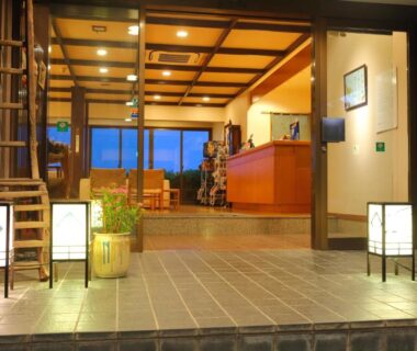 Warm tiled entrance with wooden beams, lanterns, reception counter and staircase at Onyado Satsuki