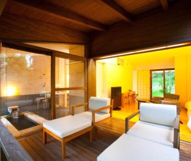 Wooden outdoor bath on ryokan deck with sliding doors opening to tatami room and lounge seating