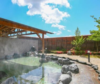 Steam rising from rock-lined outdoor onsen with wooden pergola and garden at Ooedo Onsen Monogatari Aizu Fukushima