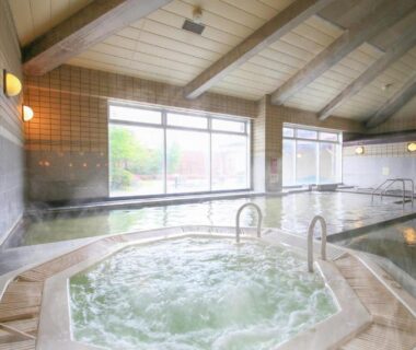 Bubbling indoor onsen bath with handrails, tiled pool and large windows at Ooedo Onsen Monogatari Aizu Fukushima
